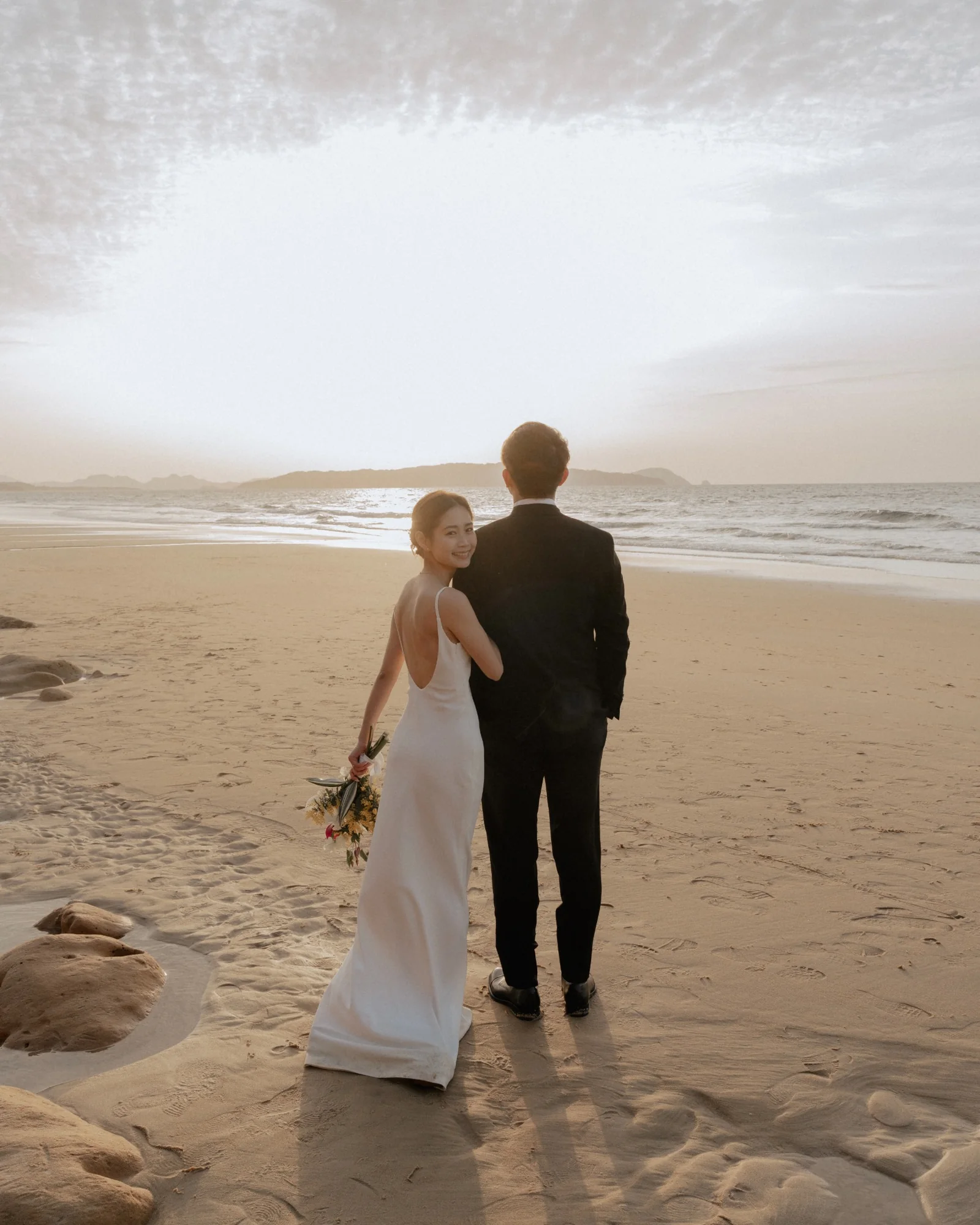 夕暮れの海辺を歩く新郎新婦